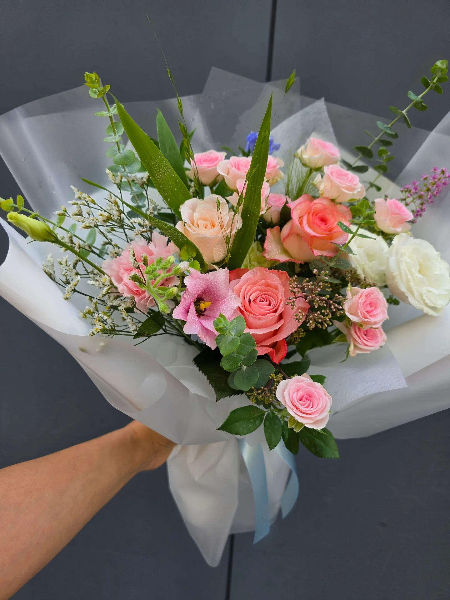 흰 포장지에 핑크 장미와 카네이션, 연한 복숭아색 꽃이 어우러진 꽃다발